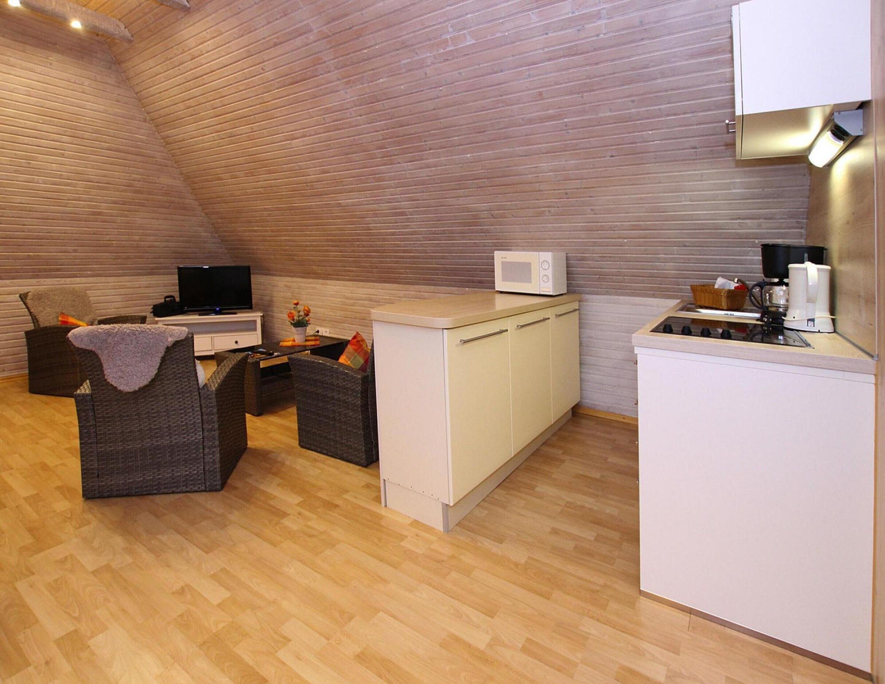 A compact kitchen with a microwave, a coffee machine, and a small dining area with wicker furniture.