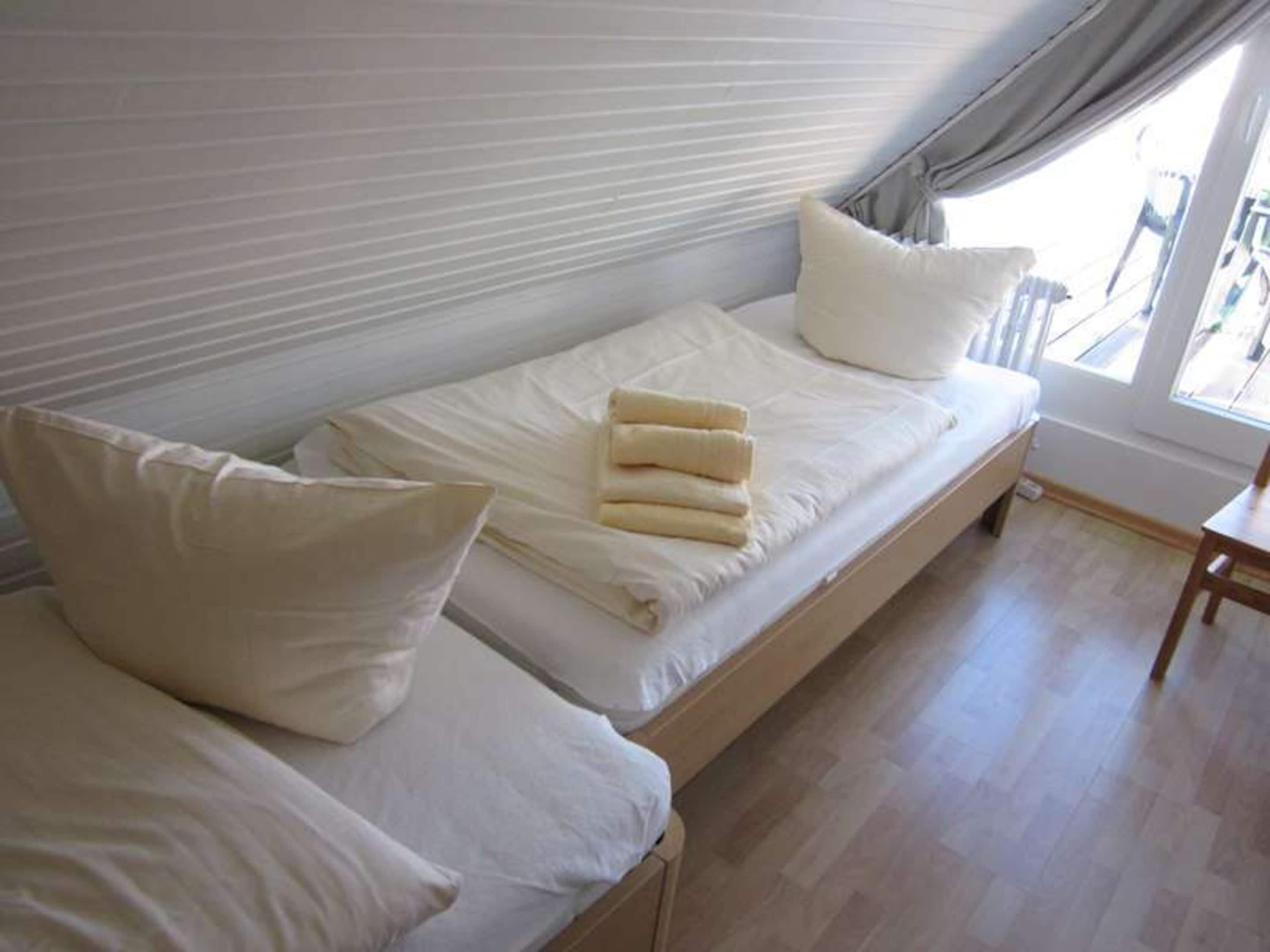 Una cama individual con ropa de cama y almohadas blancas, un cabecero de madera y una ventana con vistas al exterior.
