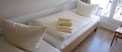 Una cama individual con ropa de cama y almohadas blancas, un cabecero de madera y una ventana con vistas al exterior.