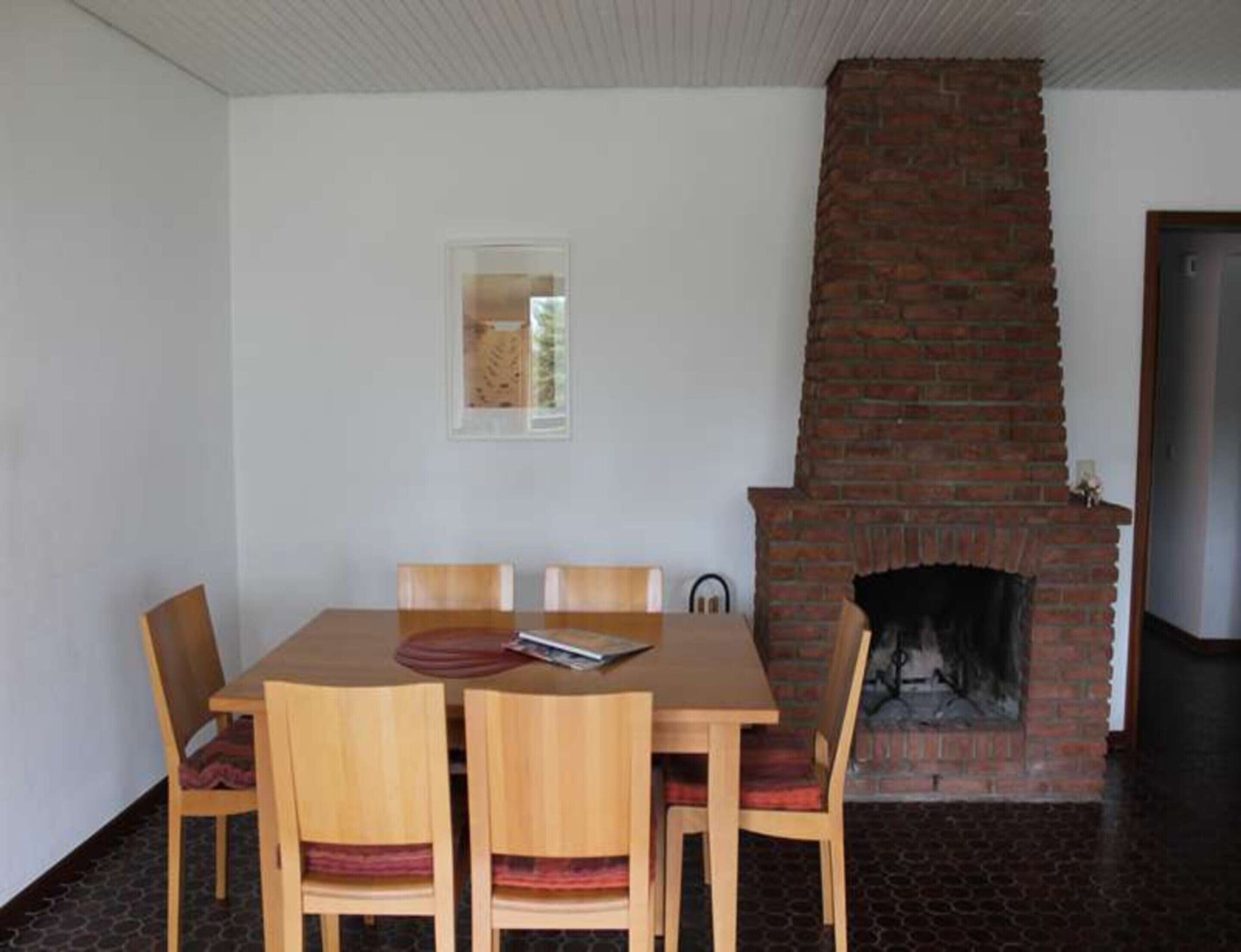Un coin repas avec une cheminée en briques, une table et des chaises en bois, et une petite fenêtre.