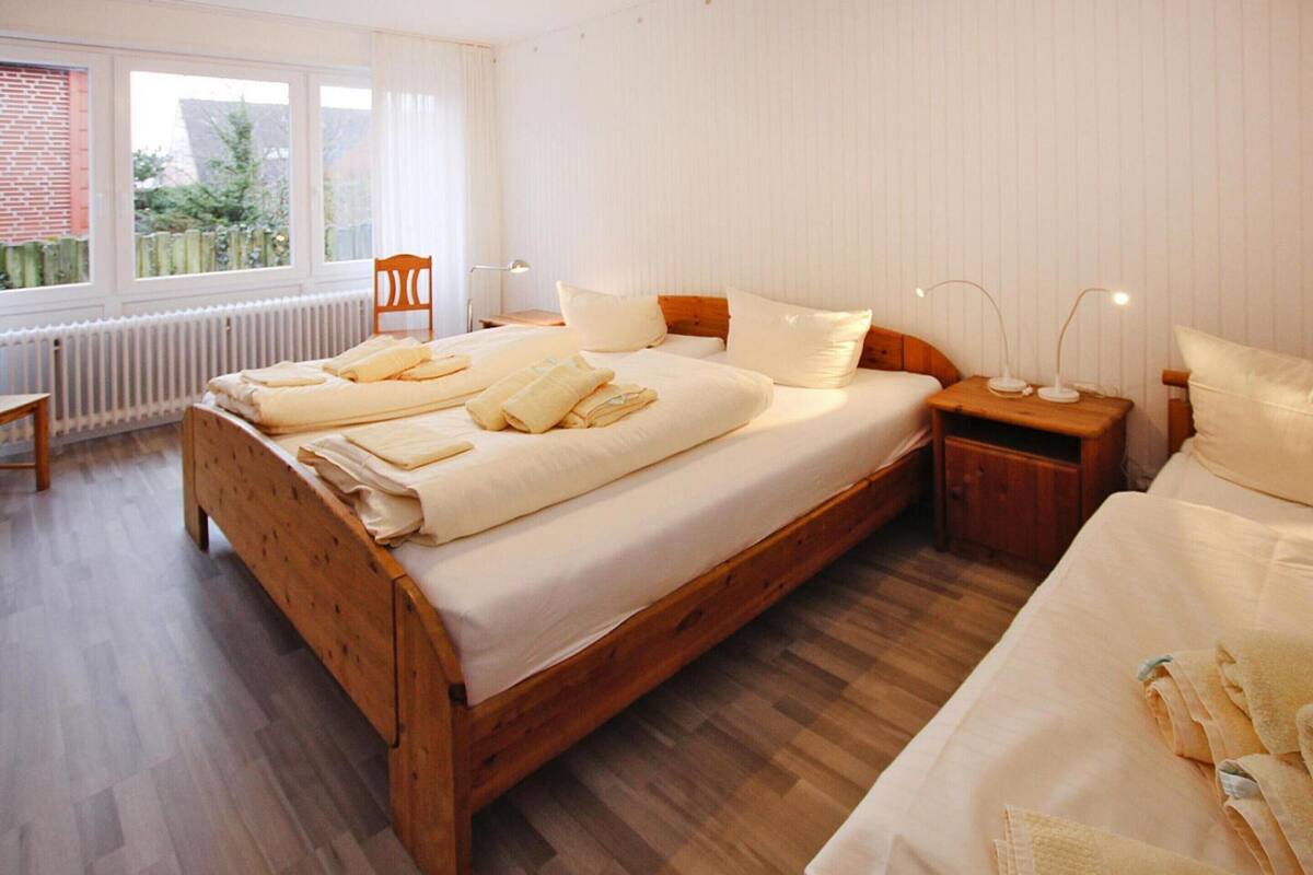 A bedroom with a wooden bed, a nightstand, a chair, and a window with curtains.