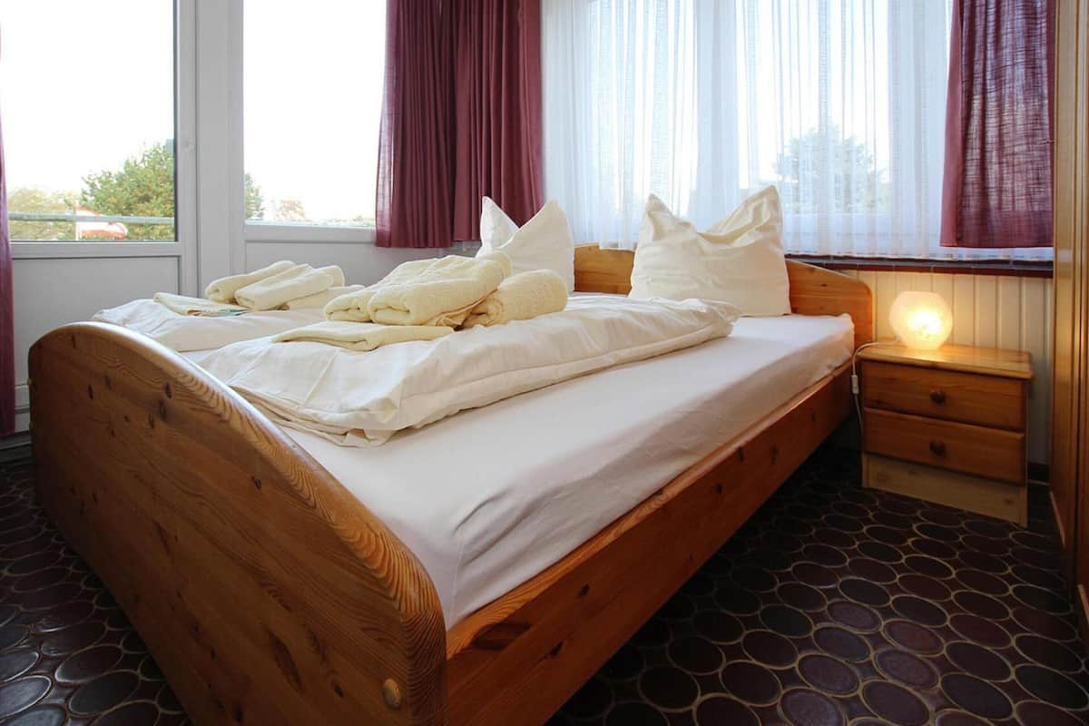 A wooden bed with white linens, a bedside table, and a window with curtains.