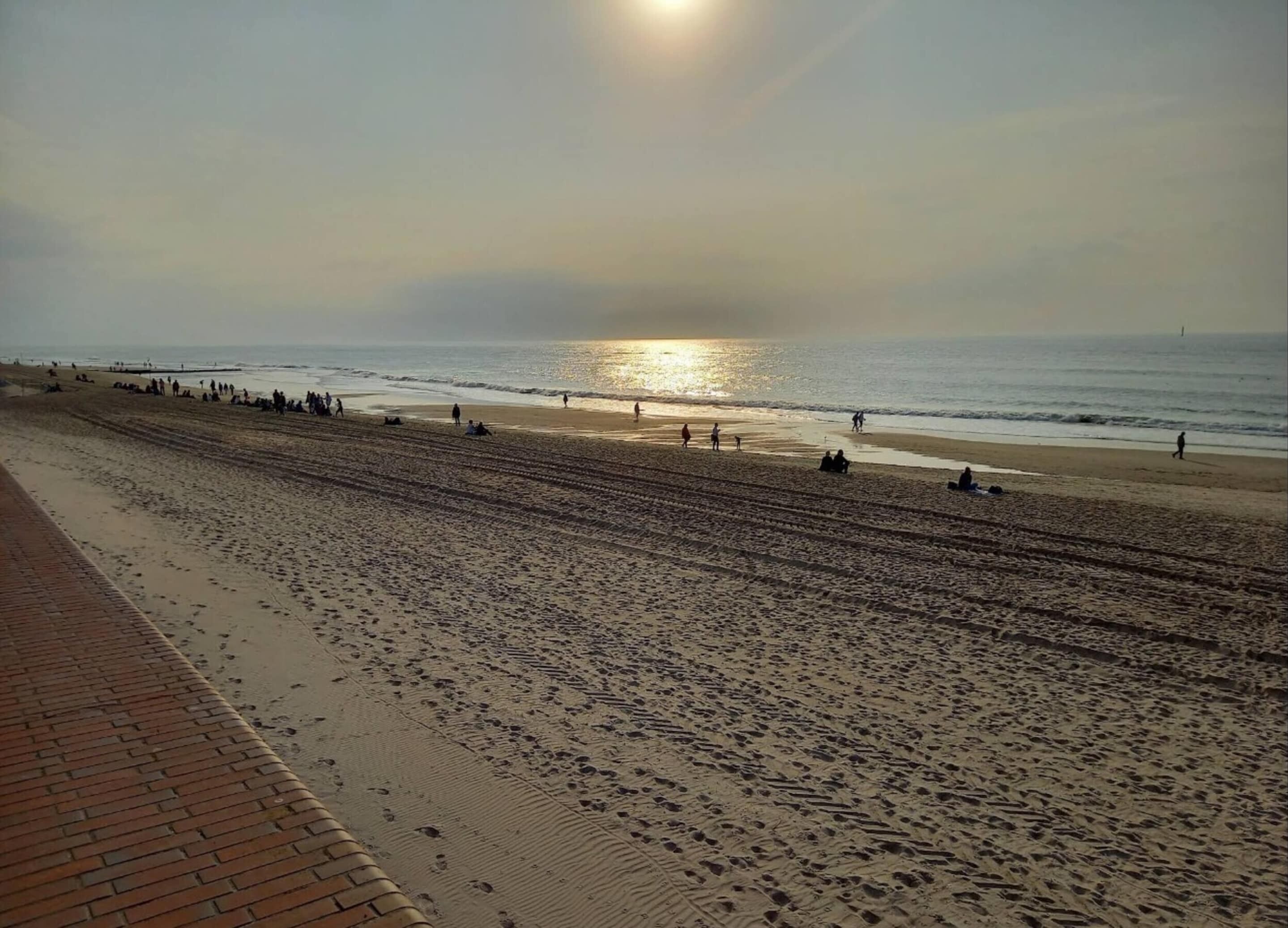 Ein Strand mit einem Pflasterweg und Menschen, die am Ufer entlanggehen.