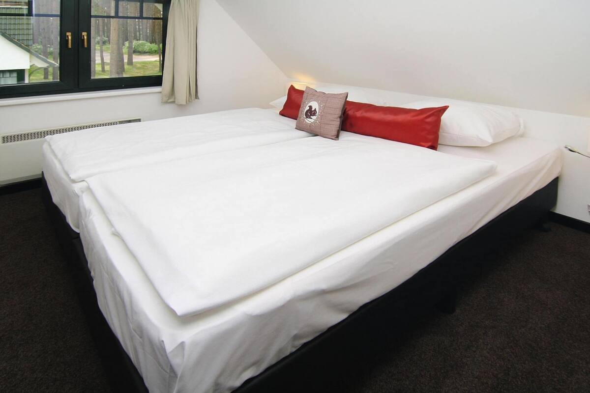 Un lit bien fait, avec du linge de lit blanc et quelques oreillers, une fenêtre avec des rideaux et un radiateur placé sous la fenêtre.