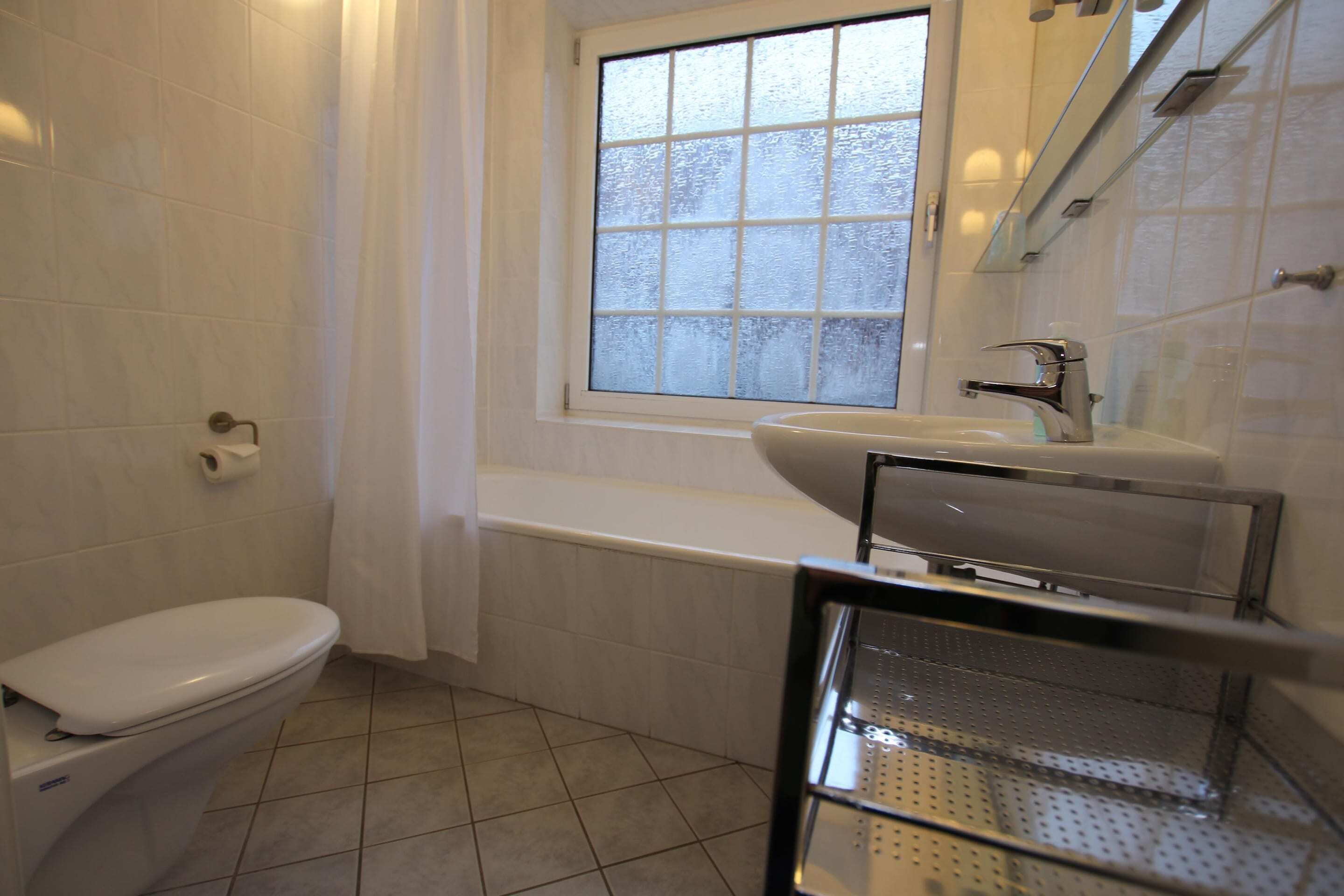 A bathroom with a toilet, a bathtub, a window, and a sink.
