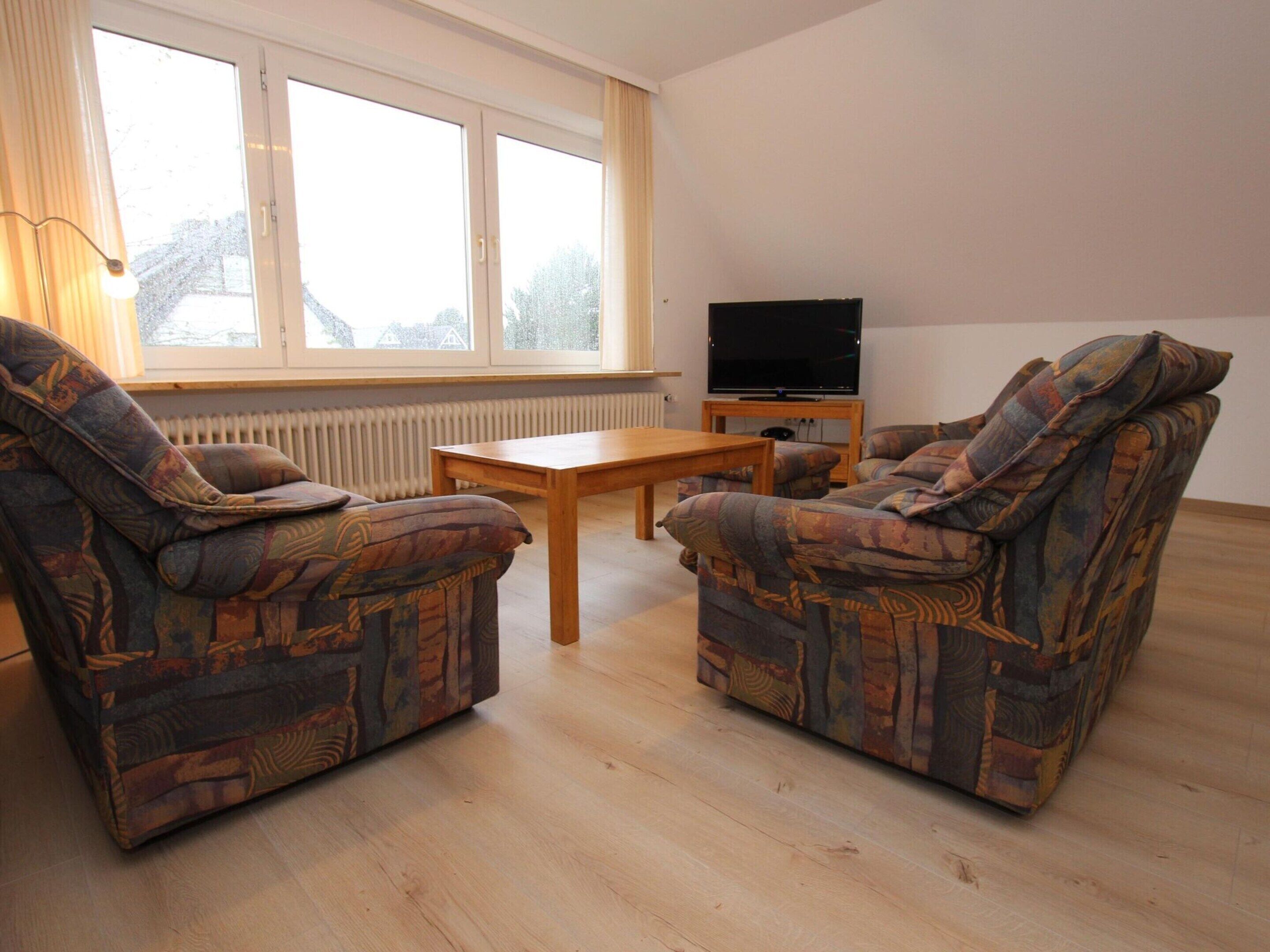 Una sala de estar con dos sillones estampados, una mesa de centro de madera y un televisor de pantalla plana sobre un mueble.