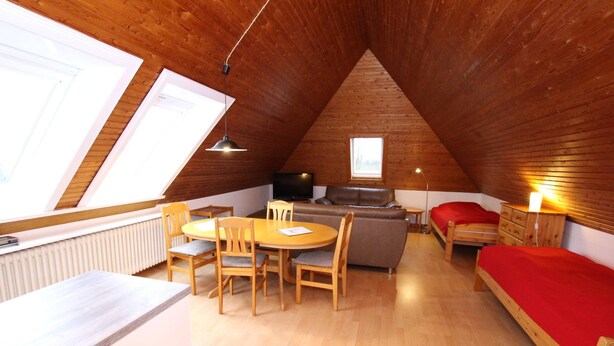 A cozy attic room with a dining table, chairs, a sofa, a bed, and a TV. - Apartment in Westerland (Sylt)