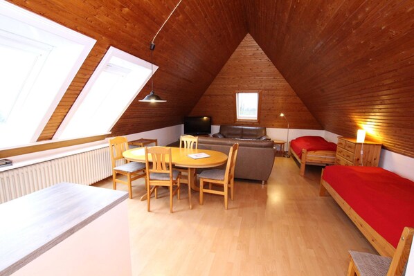 A cozy attic room with a dining table, chairs, a sofa, a bed, and a TV. - Apartment in Westerland (Sylt)