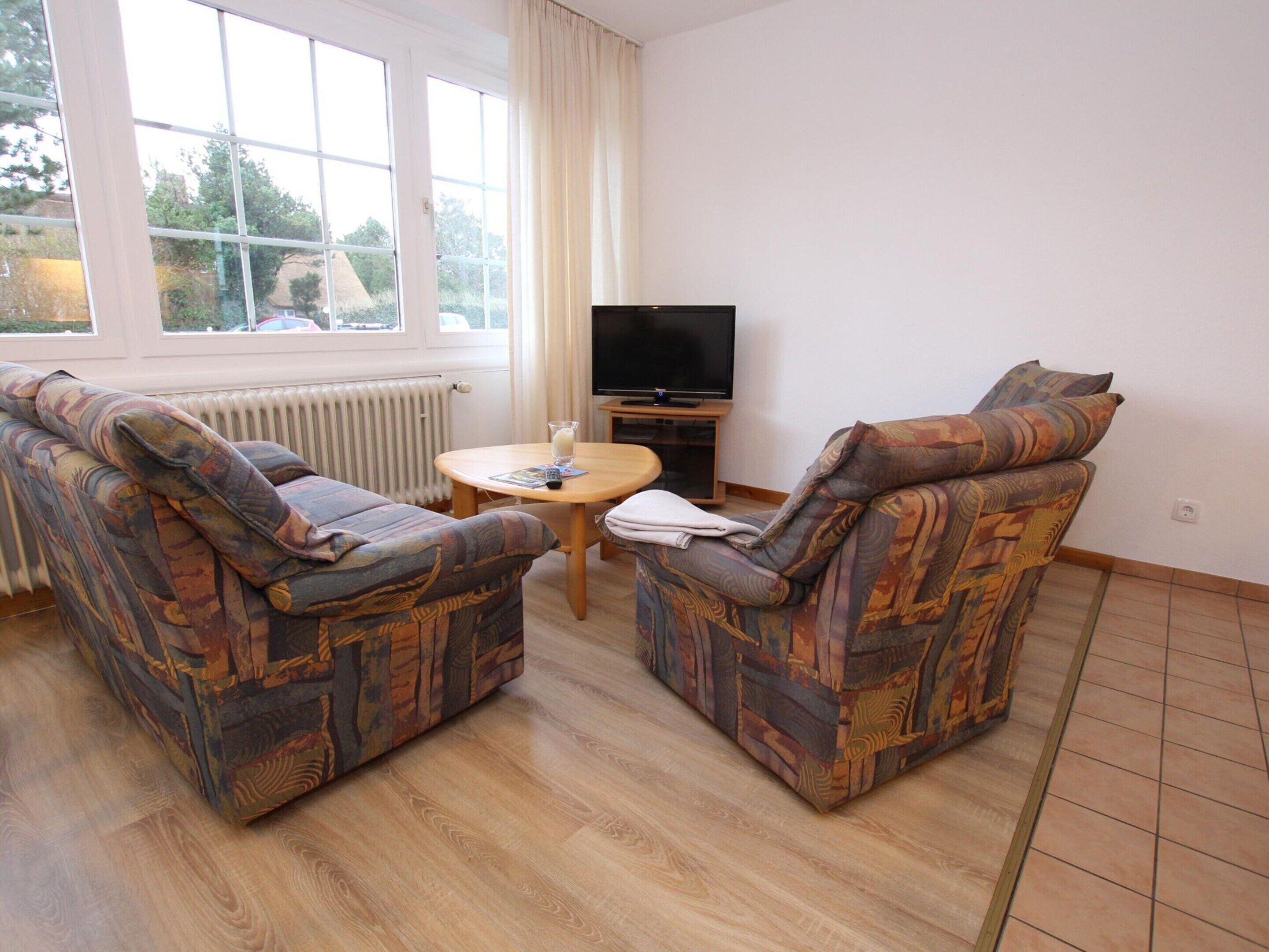 A living room with two patterned armchairs, a small round table, a television, and a window with curtains.