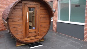 A wooden barrel-shaped structure with a door and window, placed on a tiled surface in front of a brick building with a window. - Apartment in Westerland (Sylt)