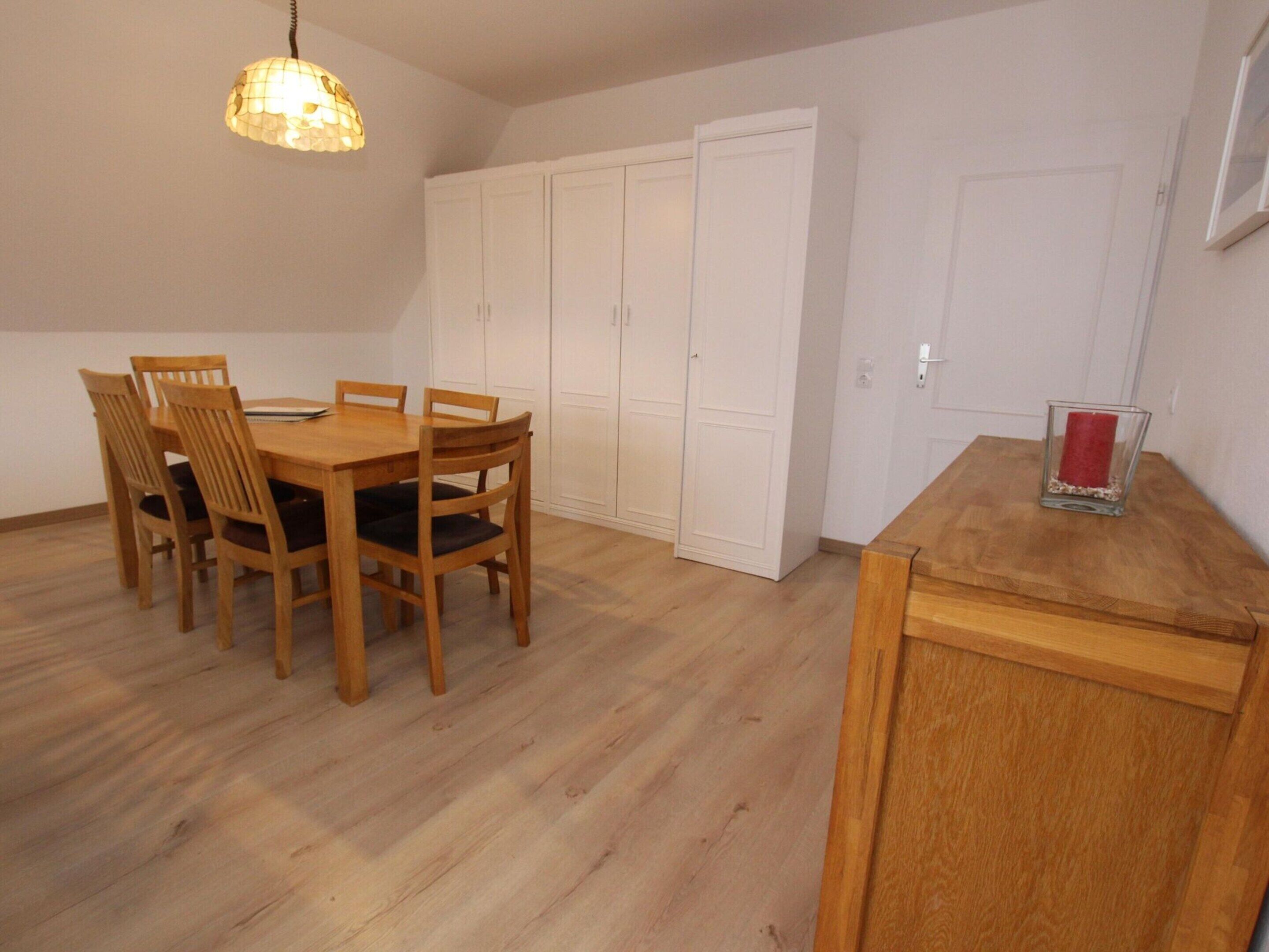 Uma sala de jantar com mesa e cadeiras de madeira, luminária pendente e armários brancos.