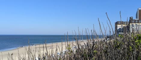 En strand med klar himmel, en sandstrand och byggnader i bakgrunden.