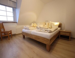 A bedroom with a wooden bed, a nightstand, a chair, and a window with blinds.