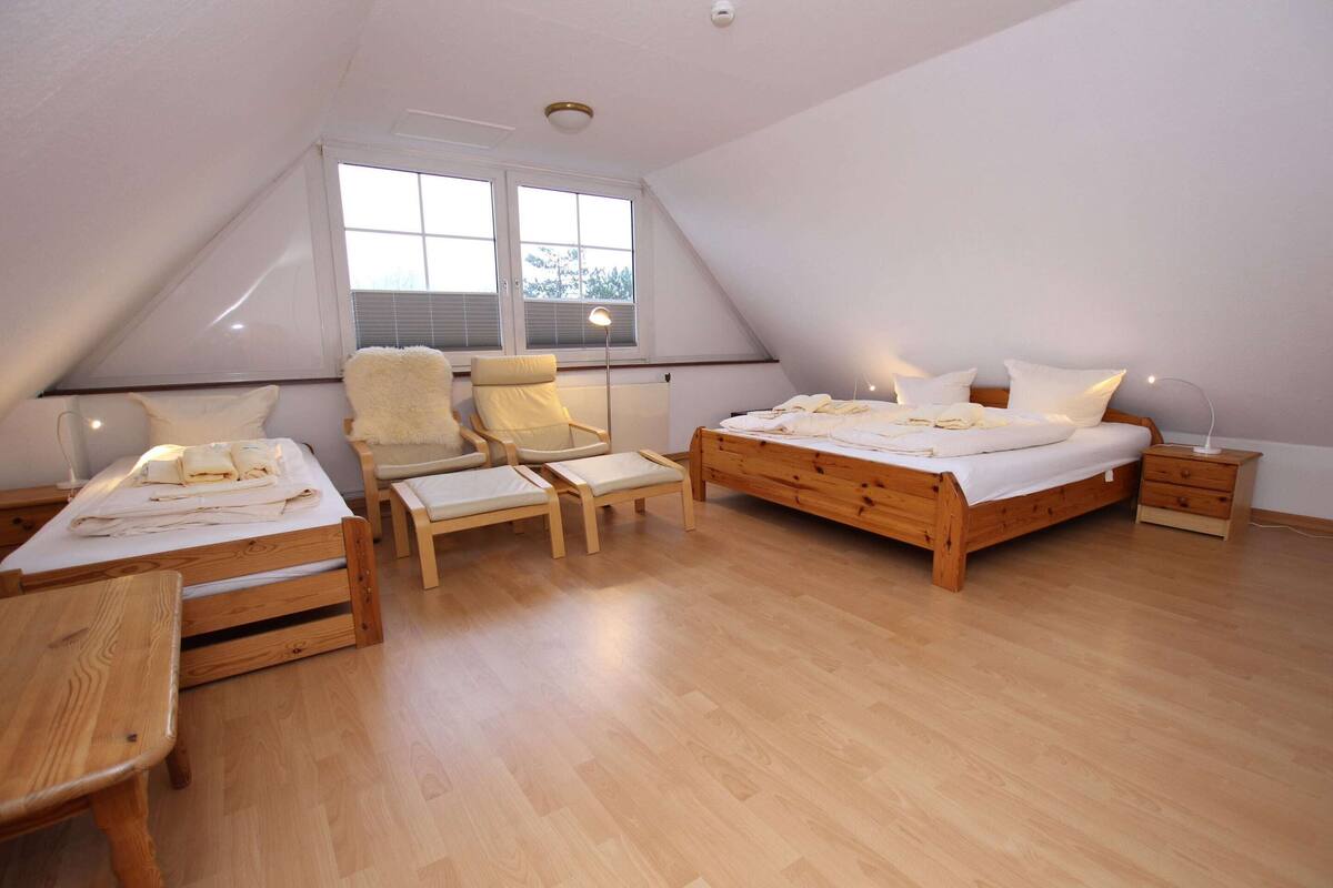 A bedroom with a sloped ceiling, a wooden bed, a chair, a small table, and a bedside lamp.