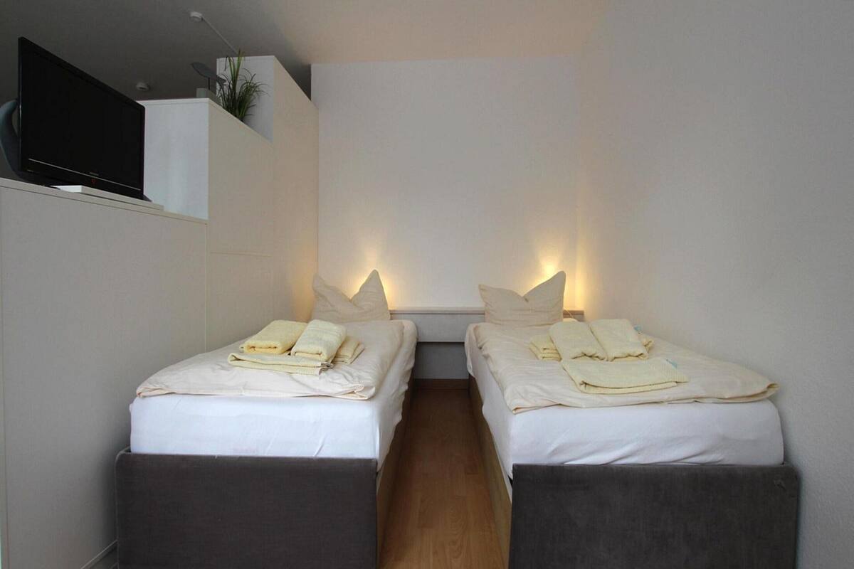 A modern hotel room with two single beds, each with a pillow and a folded towel.