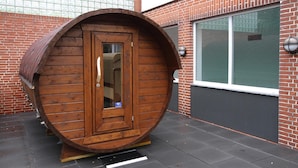 A wooden barrel-shaped structure with a door, situated on a paved area with a brick building in the background. - Apartment in Westerland (Sylt)