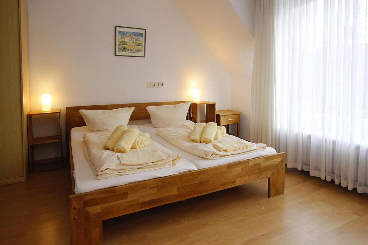 A neatly made bed with towels, a wooden headboard, bedside tables, and a painting on the wall.
