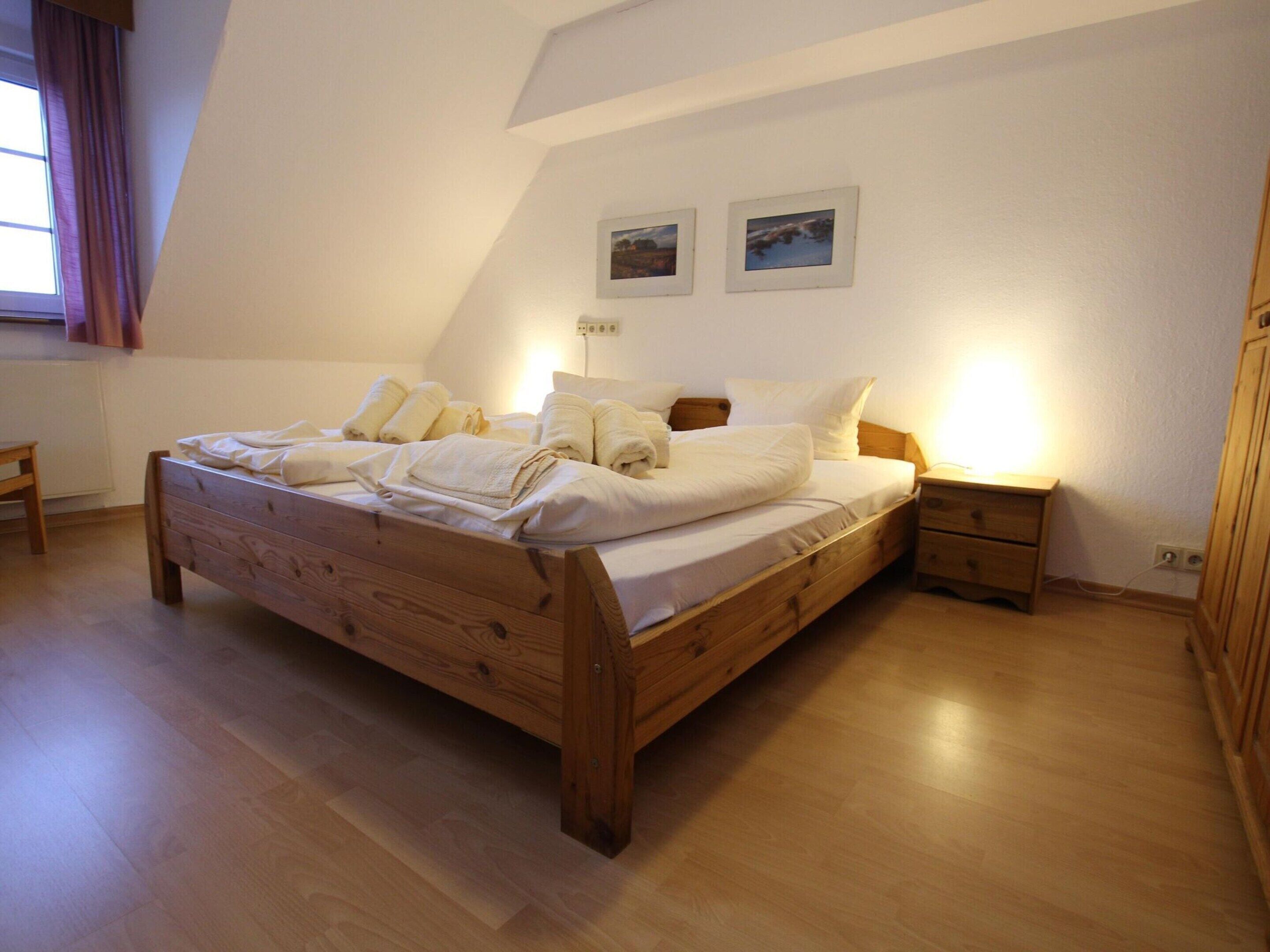 Un dormitorio con una cama de madera, una mesita de noche y una mesilla. Hay dos cuadros enmarcados en la pared sobre la cama.