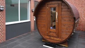A wooden barrel-shaped structure with a door, positioned on a paved surface in front of a brick building with windows. - Apartment in Westerland (Sylt)