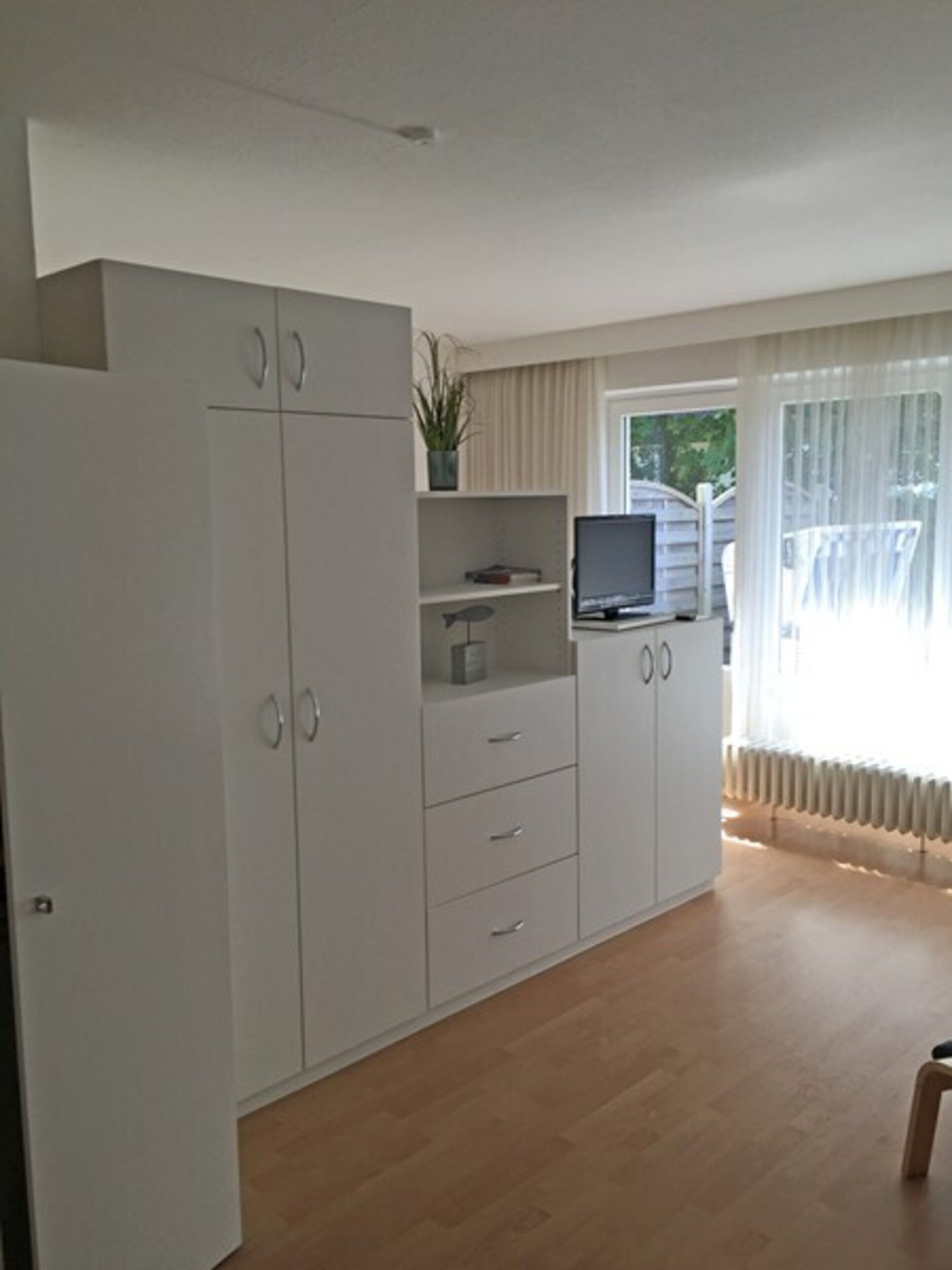 A room with a large white wardrobe, a small table with a plant, and a television on a stand.