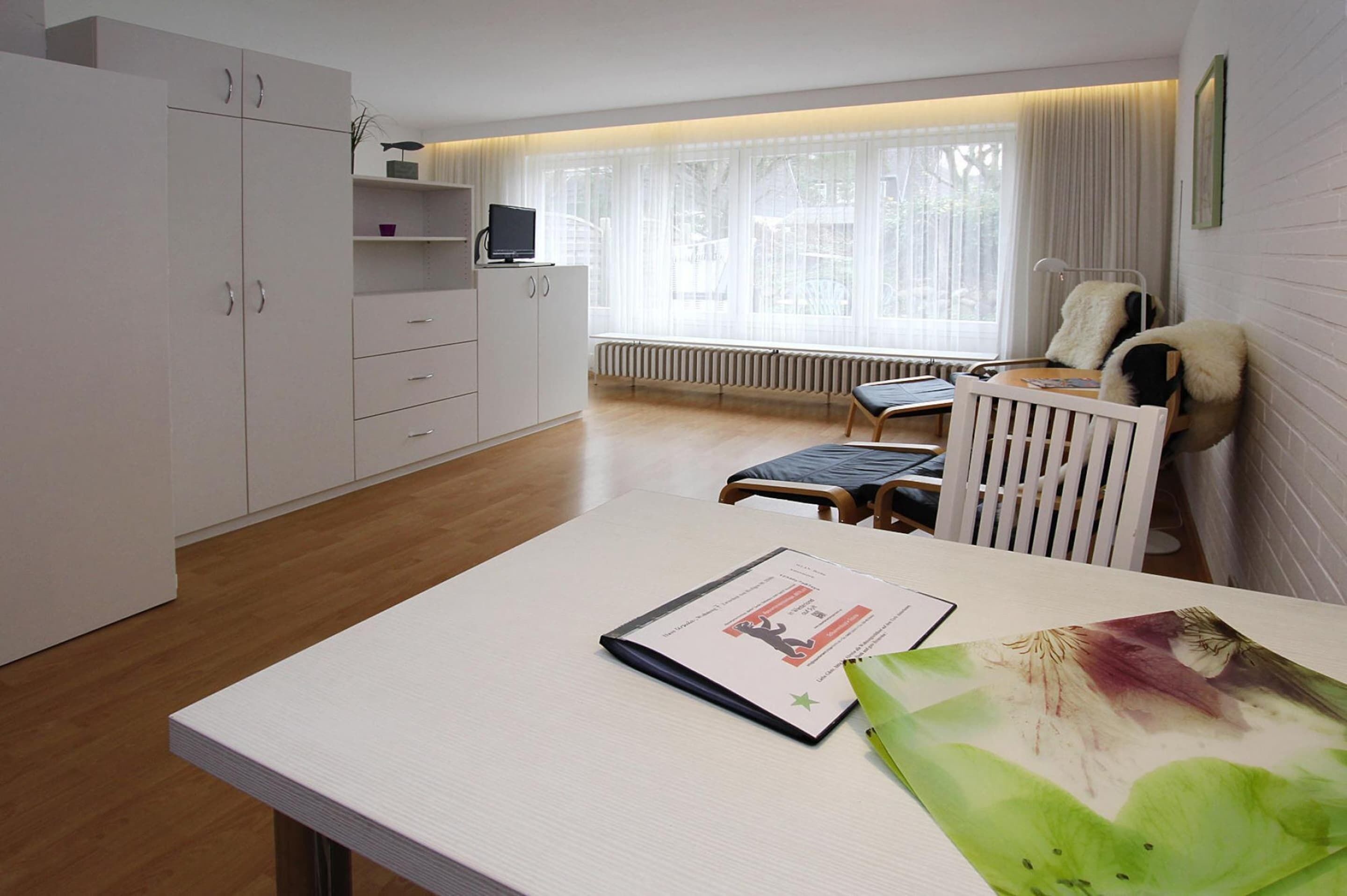 A modern room with a white table, a radiator, a window with sheer curtains, and a white chair.