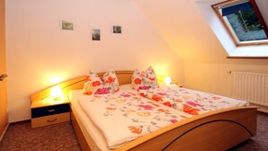 A bedroom with a wooden bed, floral bedding, a nightstand, a lamp, and a small window with a view of trees. - Apartments Spreewaldperle, Alt Zauche (Alt Zauche-Wußwerk)