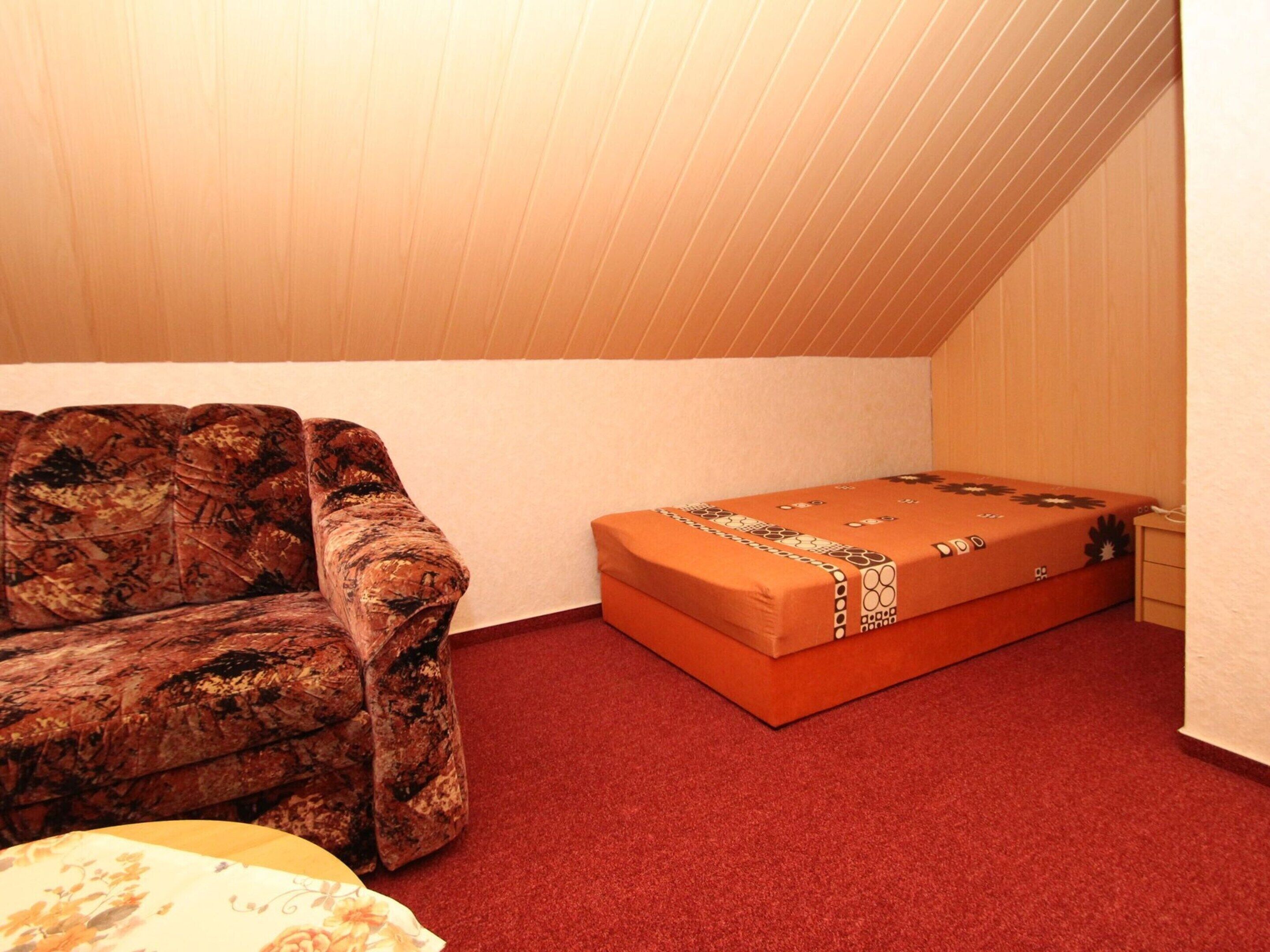 A small, carpeted room with a couch and a bed.