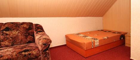 A small, carpeted room with a couch and a bed.