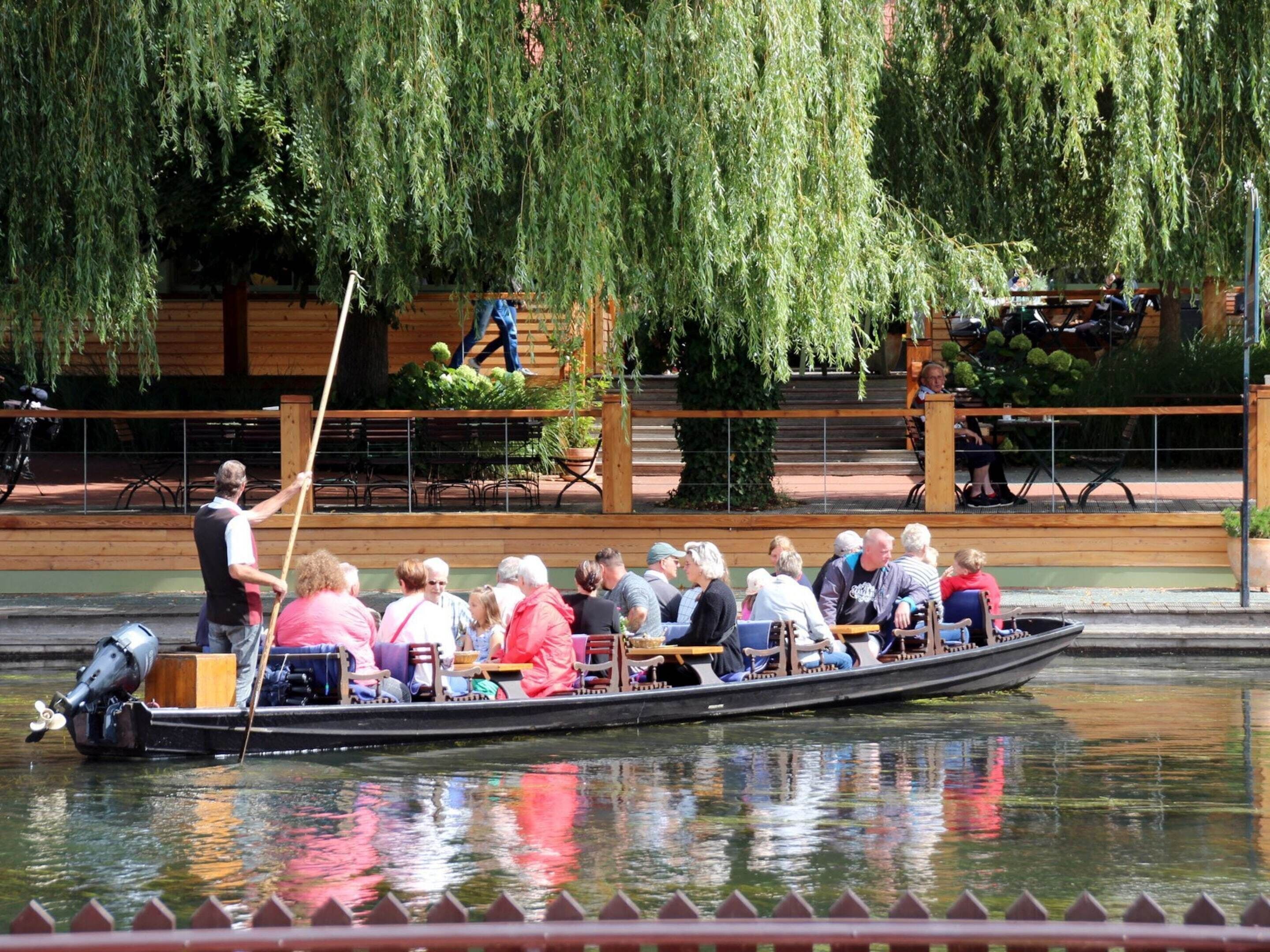 A rowboat with passengers, a man rowing, and a wooden dock with benches and a railing.