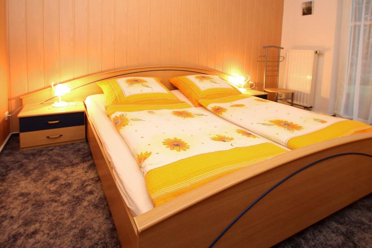 A double bed with floral bedding, a bedside table with a lamp, and a radiator in the background.