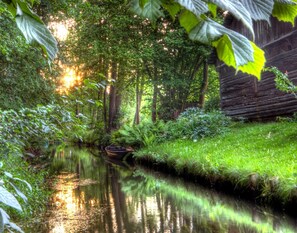 Une scène paisible au bord de la rivière, avec un bateau en bois, une végétation luxuriante et un bâtiment rustique.