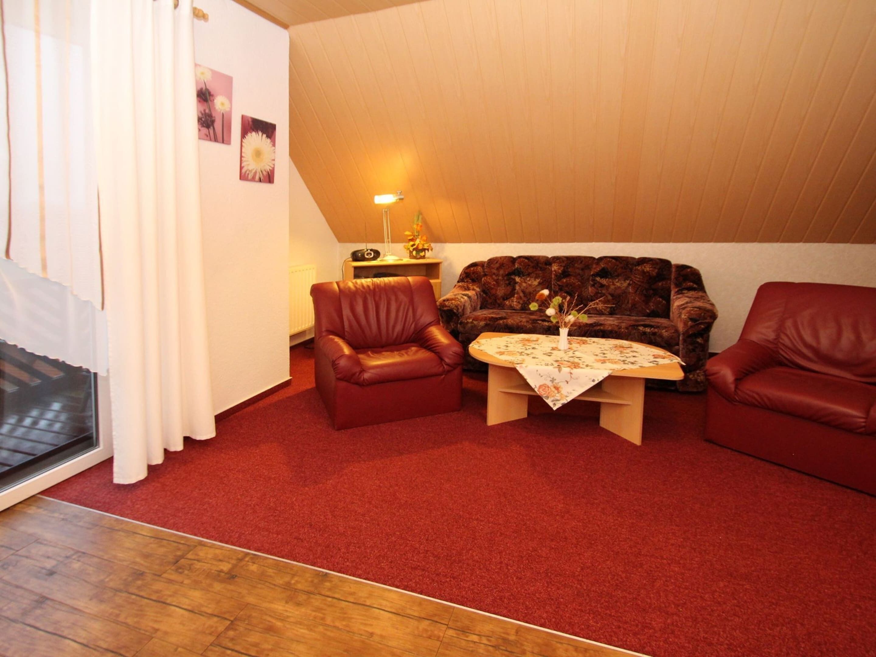 A cozy living room with a brown sofa, two red armchairs, a wooden coffee table, and a red carpet.