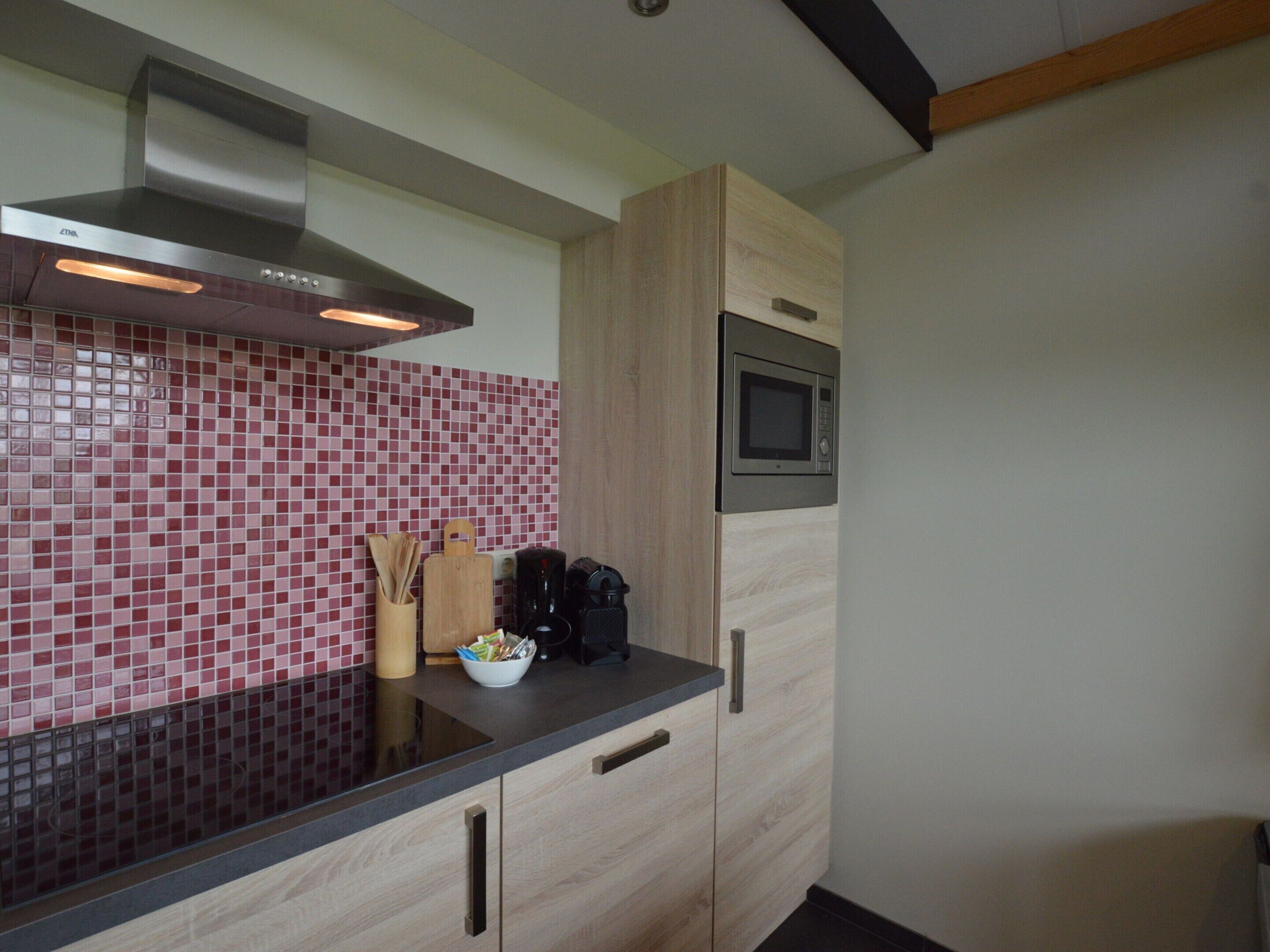 A modern kitchen with a black countertop, wooden cabinets, a microwave, and a red-tiled backsplash.
