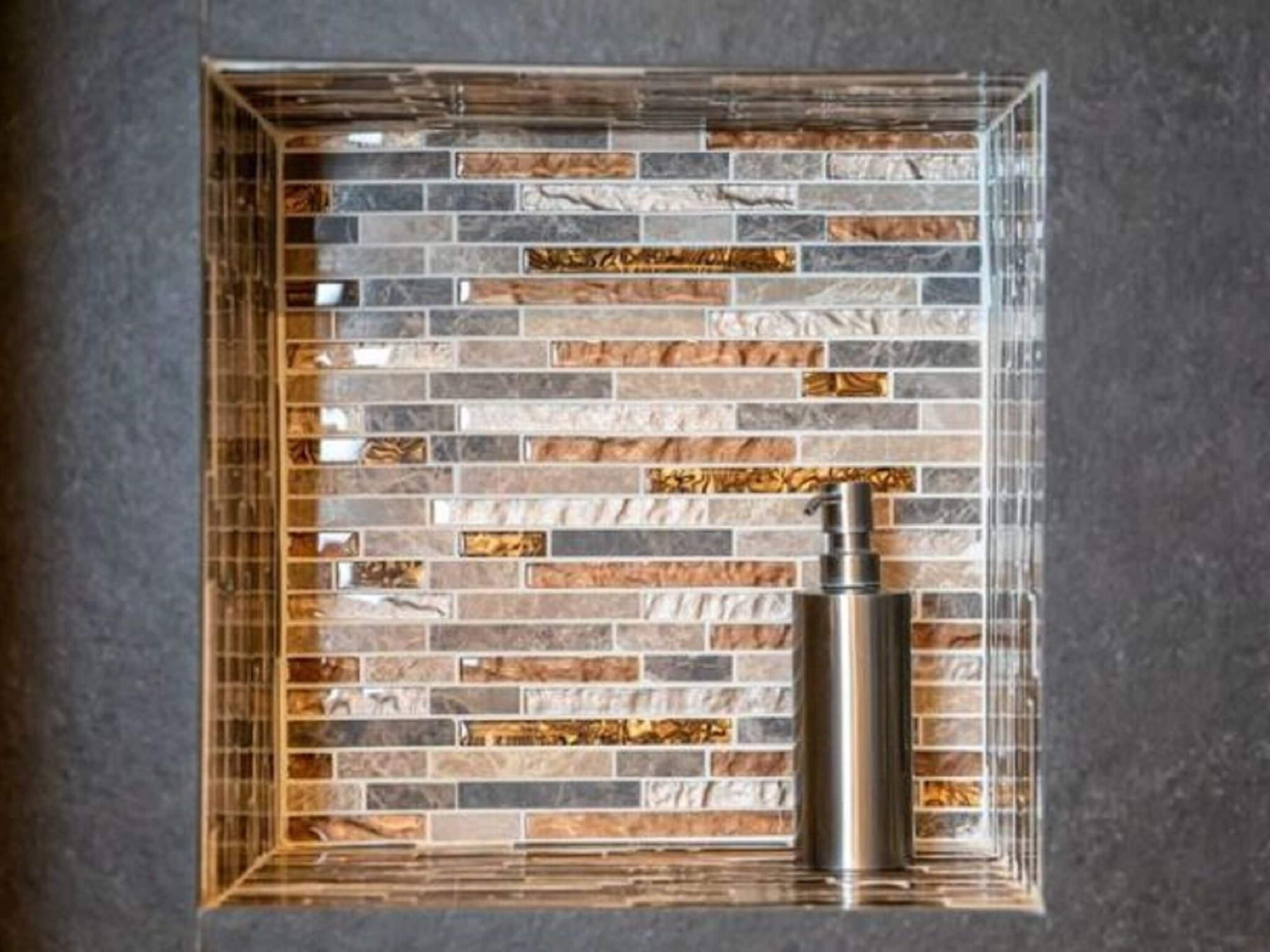 A bathroom with a tiled wall featuring a variety of stone patterns and a metallic faucet.