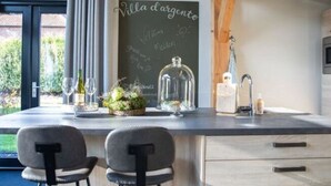 A modern kitchen with a chalkboard menu, two barstools, and a large island with a glass enclosure. - Modern & Garden-view Holiday Home in Alphen (Alphen)