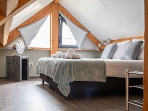 A bedroom with a sloped ceiling, a bed with a grey blanket, a bedside table with a fan, and a window with a view. - Modern & Garden-view Holiday Home in Alphen (Alphen)