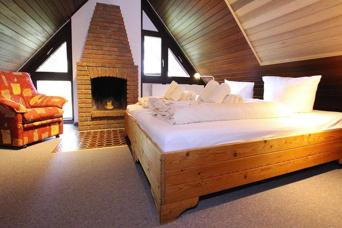 A bedroom with a wooden bed, a brick fireplace, and a red armchair.