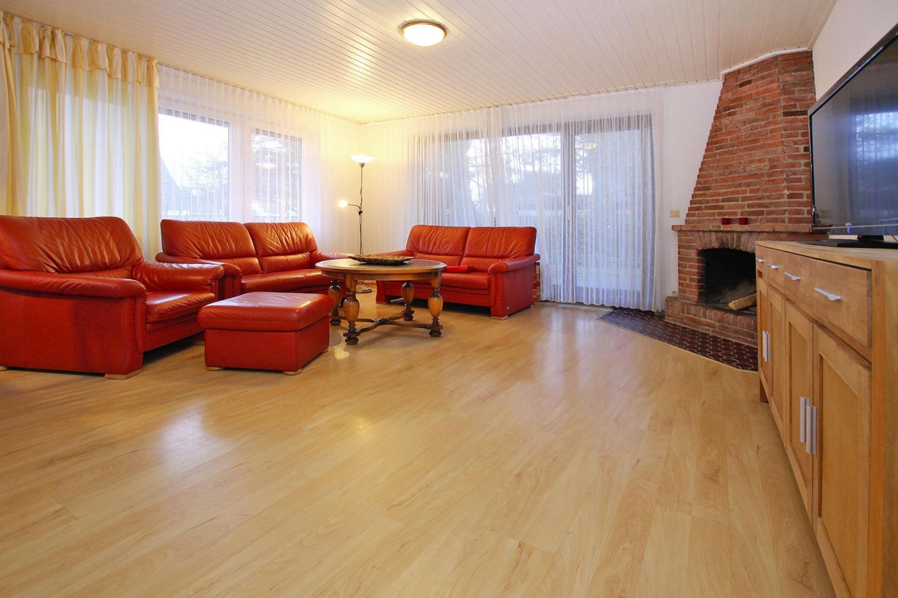 Un salon avec une cheminée en briques, des canapés en cuir, une table basse en bois et un téléviseur posé sur un meuble en bois.