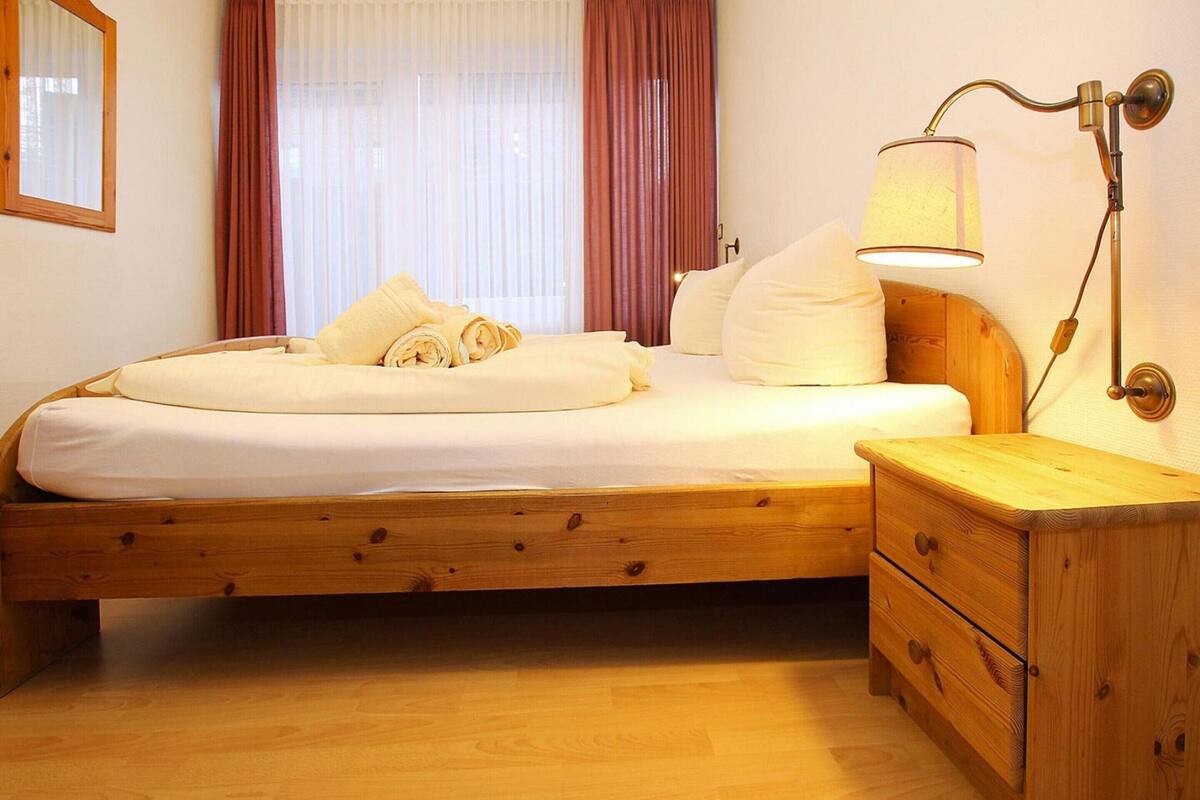 A wooden bed with white linens, a nightstand, and a wall-mounted lamp.