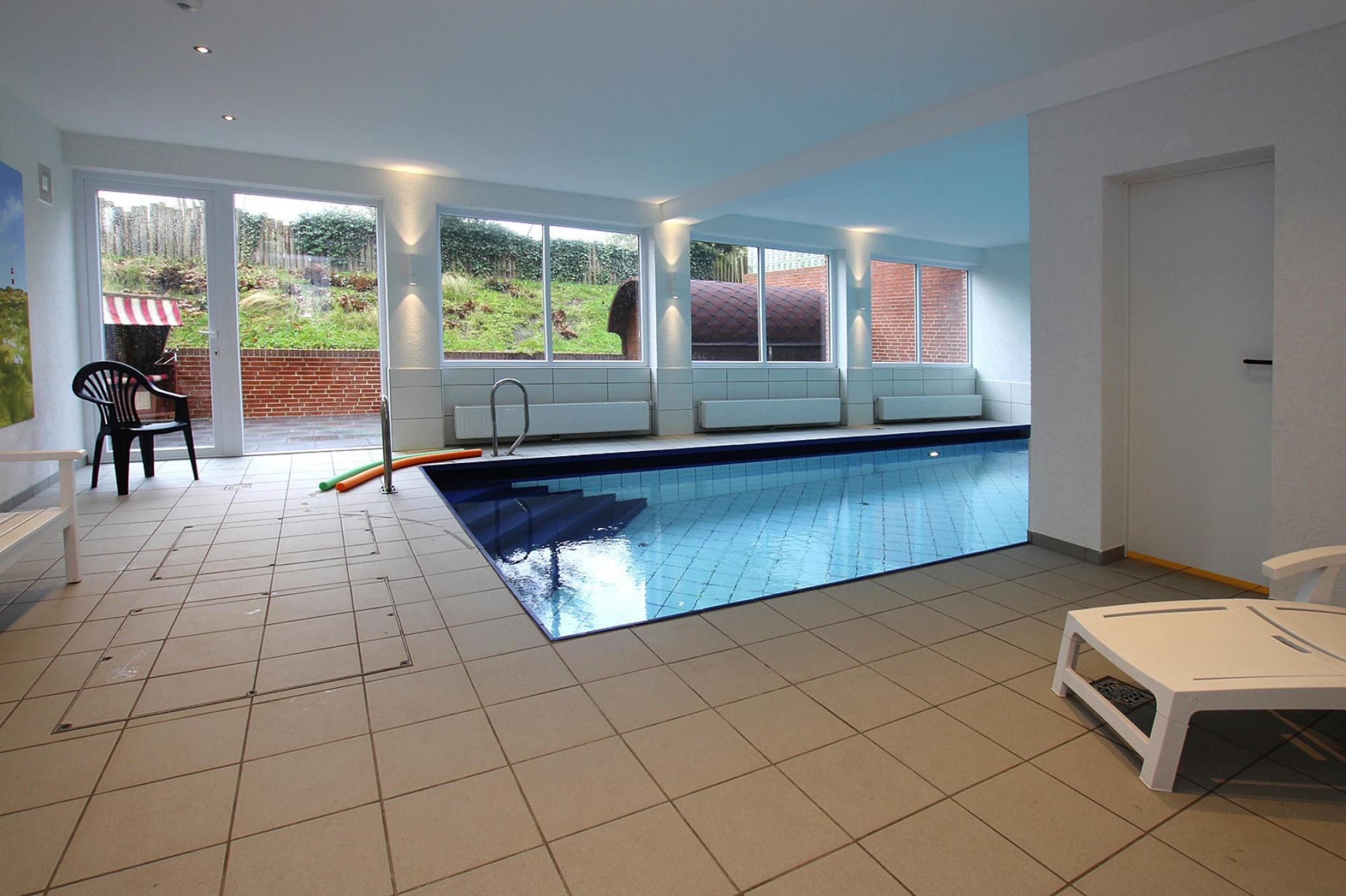 An indoor swimming pool with a view of a garden and brick wall.