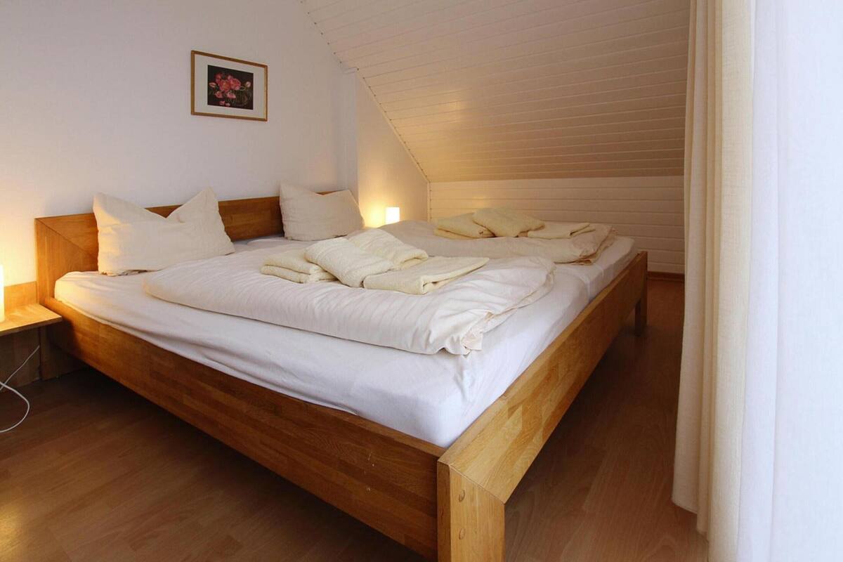 A neatly made bed with white linens and pillows, a wooden headboard, and a small bedside table with a lamp.