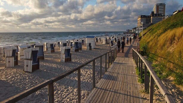 A beach with wooden boardwalks, beach chairs, and a grassy embankment. - Apartment House Katharina, Westerland (Sylt)