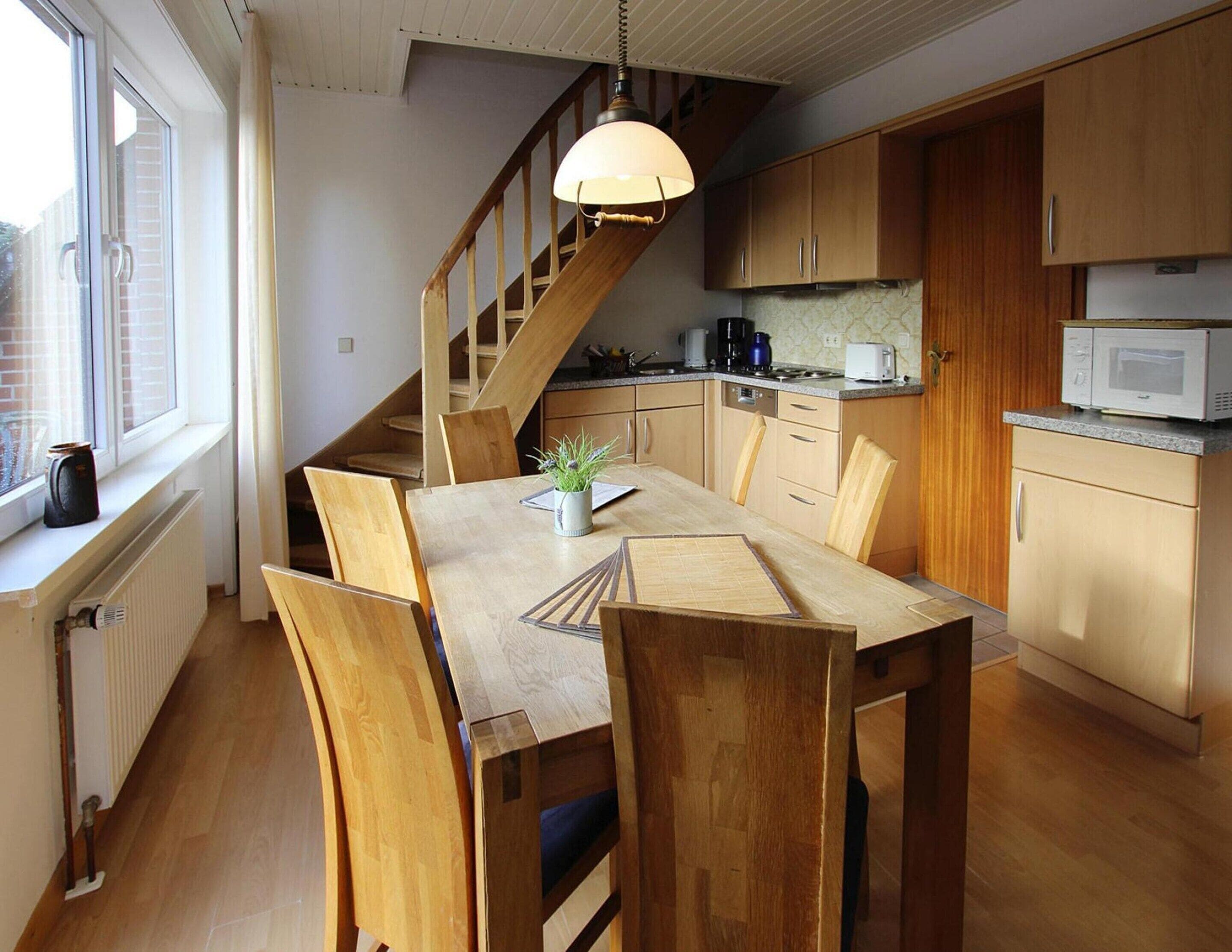 Une cuisine moderne avec des meubles en bois, une table à manger avec des chaises, un escalier et une fenêtre avec des stores.