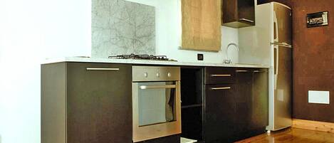 A modern kitchen with dark cabinetry, a built-in oven, a stainless steel range hood, and a refrigerator.