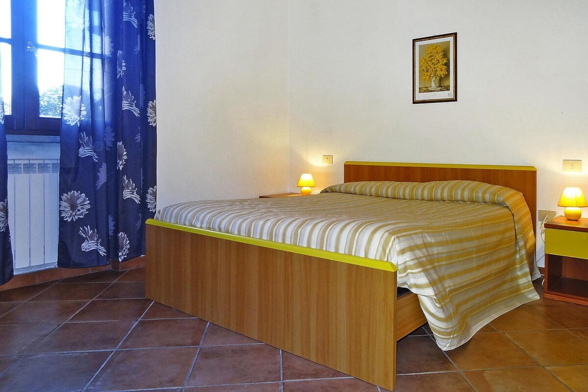 Una cama individual con estructura de madera y edredón a rayas, dos lámparas de noche, un cuadro en la pared y una ventana con cortinas azules.