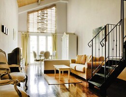Un salón espacioso con piso de madera, un sofá, una mesa de centro y una escalera con barandilla negra.