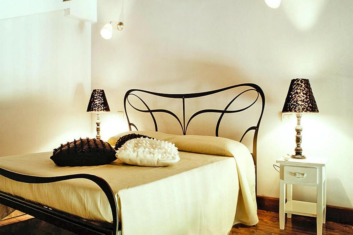 A bedroom with a metal bed frame, a bedside table, two lamps, and a bedside table drawer.