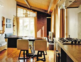 Una sala de estar acogedora con un sofá, dos sillones, un televisor y un área de cocina con estufa.