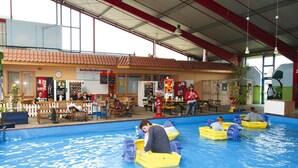 An indoor swimming pool area with children in boats, a cafeteria, and a Coca-Cola vending machine. - Seepark Burhave, Burhave (Butjadingen)