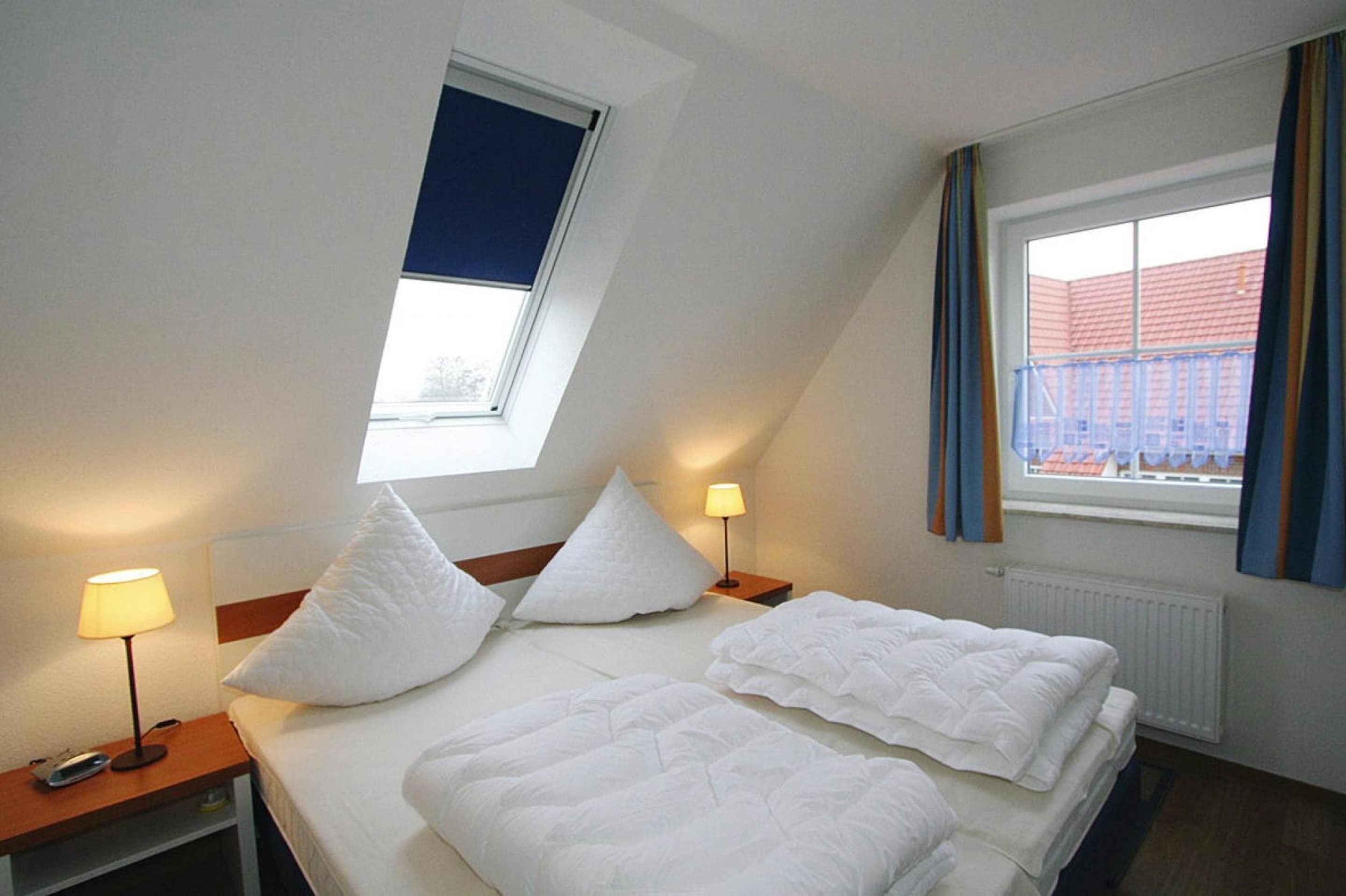 A hotel room with a bed, two bedside lamps, a window with curtains, and a view of a building outside.